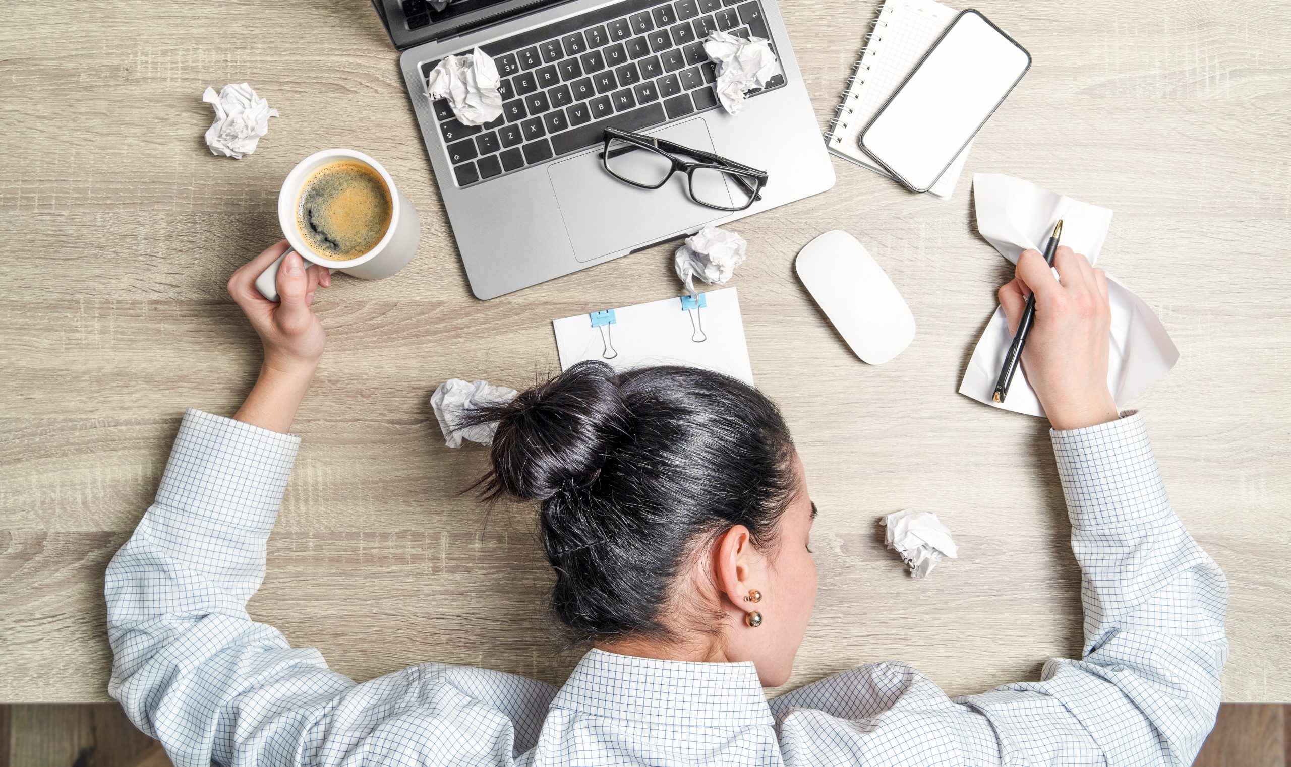 Top view of tired, overwoked businesswoman, office worker, lying on the desk with laptop, coffee and papers
